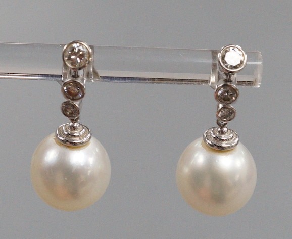 A modern pair of 750 white metal, singe stone South Sea pearl and graduated three stone diamond set drop earrings, overall 22mm, gross weight 6.8 grams